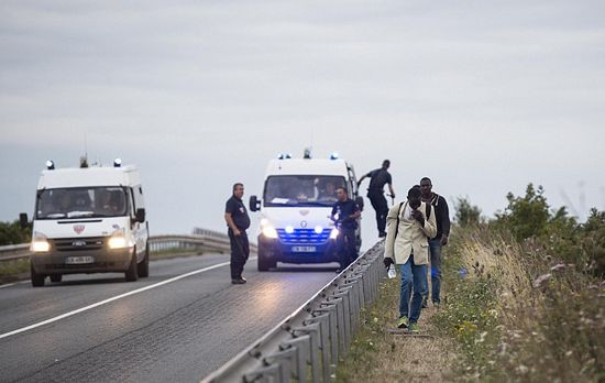 Người di cư đi dọc con đường dẫn đến đường hầm eo biển Anh trong khi cảnh sát vẫn theo dõi sát sao.