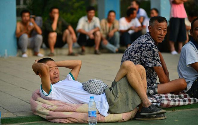 Người dân địa phương nằm, ngồi la liệt trong khuôn viên một trường học ở Thiên Tân sau khi vụ nổ tối qua khiến nhà cửa họ tan hoang. Ảnh: Cfp.