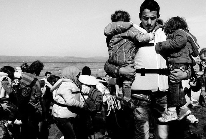 Một người đàn ông mang quốc tịch Syria bế trên tay 2 đứa con sau khi thuyền cập bến.