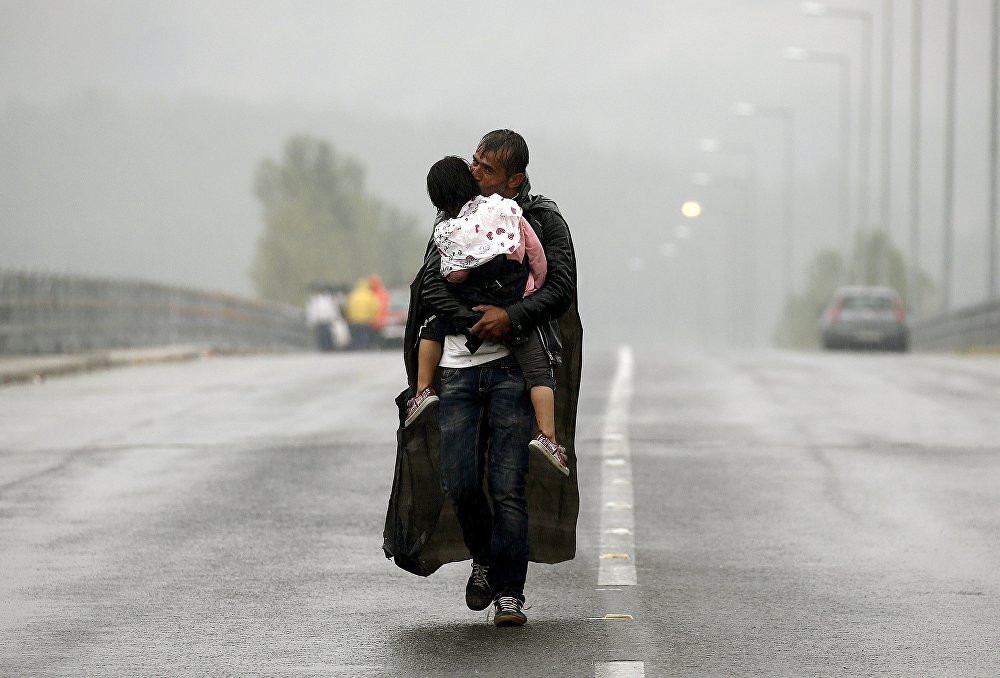 Một người di cư Syria hôn con gái khi đi bộ trong màn mưa bão để hướng về khu vực biên giới của Hy Lạp với Macedonia, gần ngôi làng Idomeni của Hy Lạp hôm 10/9.