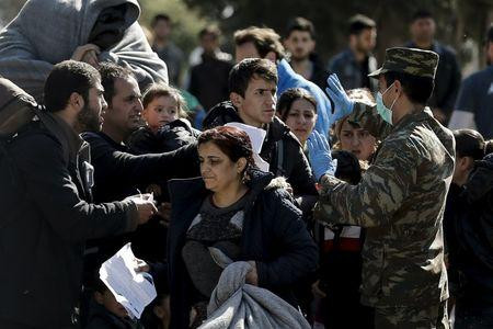 Một sỹ quan quân đội Hy Lạp (phải) kiểm tra giấy tờ của người di cư trước khi cho họ rời khu trại dành cho người di cư và đi tới biên giới Hy Lạp - Macedonia tại Schisto, gần Athens, Hy Lạp hôm 23/2. Ảnh: Reuters.