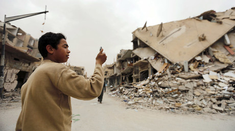 Cậu bé chụp ảnh các tòa nhà bị hư hại khi trở về thăm thành phố Palmyra hôm 9/4. Ảnh: Reuters.