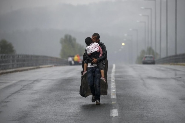 Một người đàn ông Syria ôm con gái và đi về phía biên giới Hy Lạp – Macedonia dưới cơn mưa lớn ngày 10/9/2015. Ảnh: Reuters