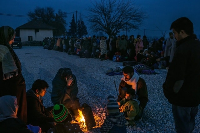 Một gia đình người tị nạn từ Syria sưởi ấm quanh đống lửa trong khi những người khác xếp hàng đăng ký tại một trại tiếp nhận ở Gevgelija, Macedonia, ngày 21/11/2015. Ảnh: New York Times