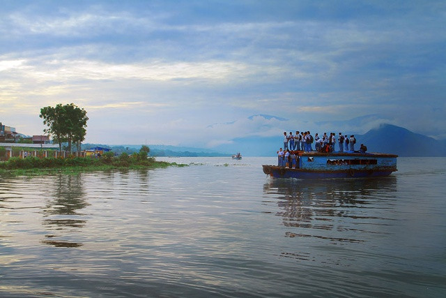 Trẻ em đứng trên nóc thuyền để qua sông đi học ở Panguruna, Indonesia. Ảnh: Muhamad Buchari.