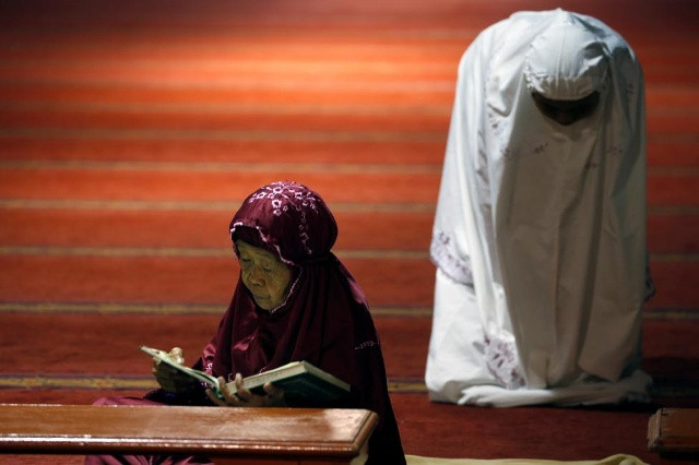 Một phụ nữ Hồi giáo chăm chú đọc kinh Koran, trong khi người còn lại thành tâm nguyện cầu trong ngày đầu tiên của tháng Ramadan tại đền thờ Istiqlal ở Jakarta, Indonesia hôm 6/6.