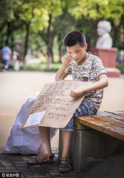 Cậu bé đeo trước ngực một tấm bìa có ghi dòng chữ: 