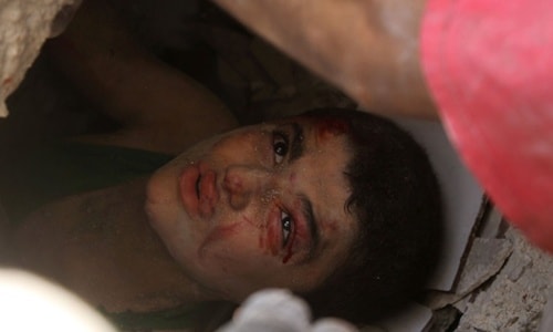 Bé trai bị kẹt dưới đống đổ nát sau một đợt oanh kích ở Aleppo hôm 25/7. Ảnh:AFP