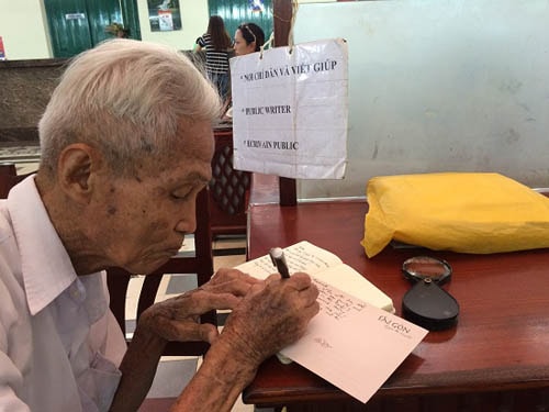 Ông Dương Văn Ngộ cẩn trọng dùng kính lúp đọc từng câu chữ của khách rồi dịch và viết thư. Ảnh: Mỹ Phượng