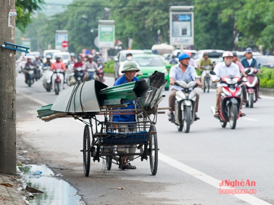 Ngay trước bến xe khách TP Vinh, một người đàn ông đang xoay xở với những tấm tôn được cuộn tròn bằng dây giun mỏng manh  nơi phương tiện giao thông đông đúc