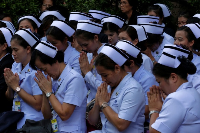 Các y tá chắp tay cầu nguyện khi họ chờ bên vệ đường, trong lúc linh cữu Quốc vương Bhumibol Adulyadej được đưa từ bệnh viện ở Bangkok tới Hoàng cung. Ông qua đời hôm qua tại bệnh viện ở tuổi 88, chấm dứt 7 thập kỷ trị vì.
