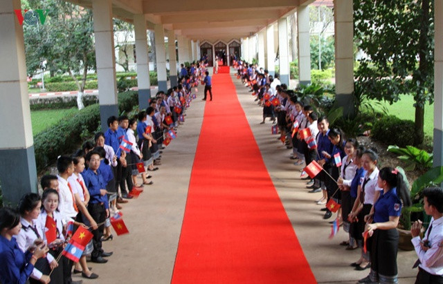 Hàng trăm sinh viên, học sinh cầm quốc kỳ hai nước Lào - Việt Nam đứng dọc hành lang của trường ĐHQG Lào đón Tổng Bí thư Nguyễn Phú Trọng và Đoàn đại biểu cấp cao Việt Nam đến thăm trường.