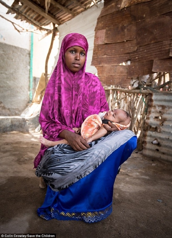 Khadra, 16 tuổi, bế con gái hai tháng tuổi trong nhà ở Somalia. Theo tổ chức Save the Children, chiến tranh và đói nghèo đã làm gia tăng số lượng các vụ bé gái kết hôn với đàn ông lớn tuổi, vì gia đình không thể bảo vệ hoặc nuôi sống các em. 