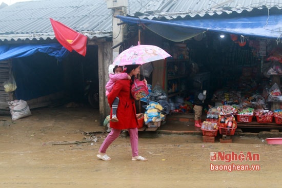 Mẹ đưa con đi chợ phiên trong cơn mưa nhẹ.