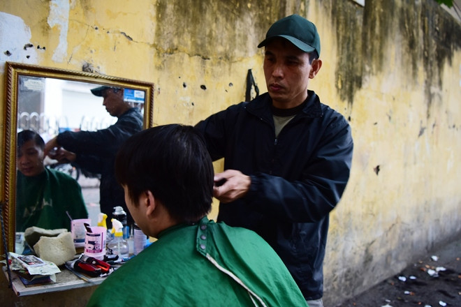 Anh Tiến Dũng ở phố Trịnh Hoài Đức cắt tóc cho khách chiều cuối năm. Dọc theo dãy phố nơi anh Dũng làm có nhiều hàng cắt tóc, nhưng giờ này chỉ còn mình anh làm việc, và có khá nhiều khách xếp hàng chờ đến lượt mình.