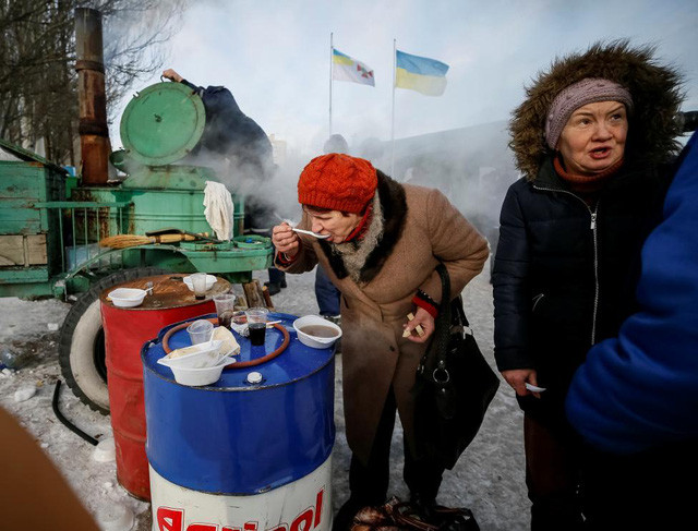 Một phụ nữ đứng ăn giữa trời lạnh trung tâm tạm trú. (Ảnh: Reuters)