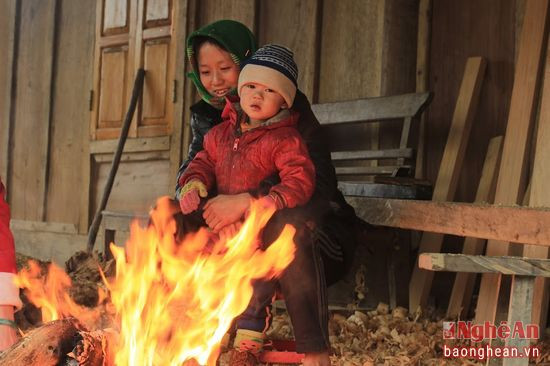 2 mẹ con người Mông này ngồi bên hiên nhà, đốt lên bếp lửa từ củi khô và vỏ bào để sưởi ấm. Bà mẹ còn rất trẻ, ôm chặt con mình trong vòng tay.
