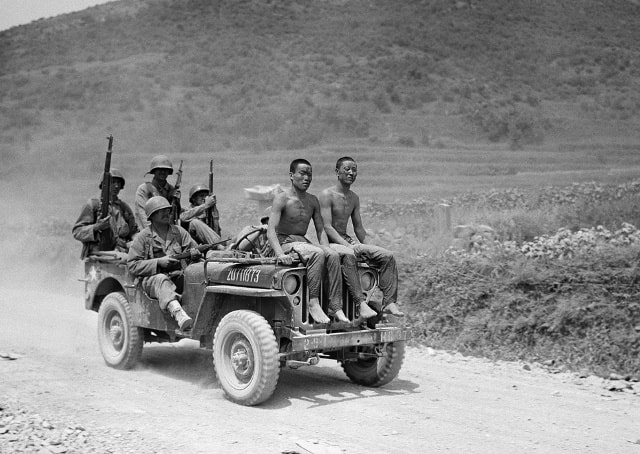 Hai tù nhân Bắc Triều Tiên bị bắt trong cuộc chiến tại Yongsan ngày 2/9/1950 ngồi trên mui xe jeep dưới sự giám sát của lính Mỹ thuộc Sư đoàn bộ binh số 2. Ảnh: AP.