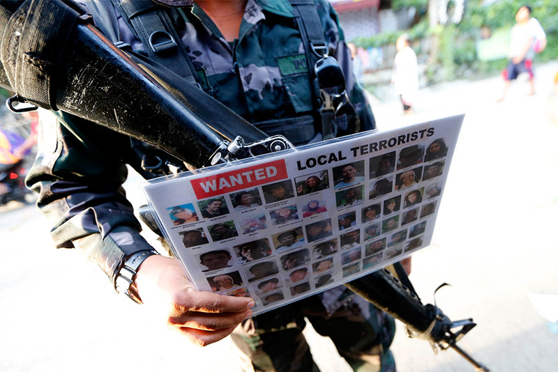 Cảnh sát cầm theo tấm poster trong đó có mặt của các tay súng phiến quân Maute bị truy nã. Ảnh: AP