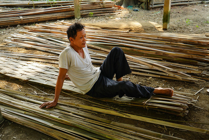 Công việc đan liếp phải ngồi lâu, dễ mỏi. Đây là phút thư giãn ngay trên tấm liếp vừa mới đan. Ảnh: Hồ Chiến