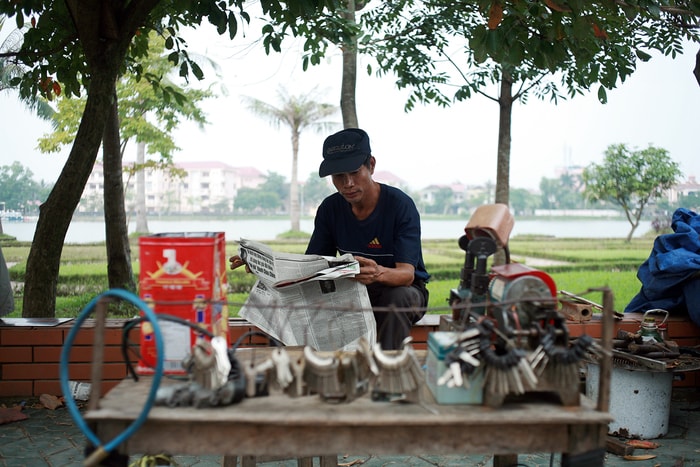 Người thợ sửa khóa đọc báo bên cạnh Hồ Goong. Ảnh: Sách Nguyễn