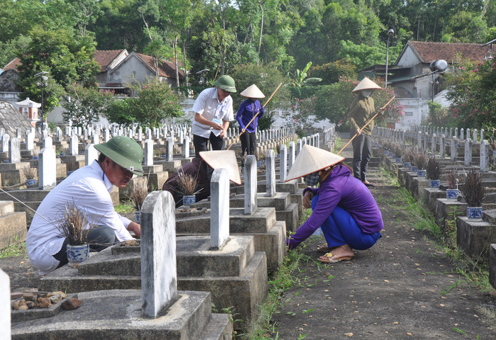 Nhân viên BQL Nghĩa trang Việt - Lào quét dọn và nhổ cỏ quanh các phần mộ liệt sỹ. Ảnh: Công Kiên