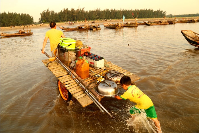 Con trai giúp bố đẩy dụng cụ đi biển vào bờ. Ảnh: Trần Cảnh Yên