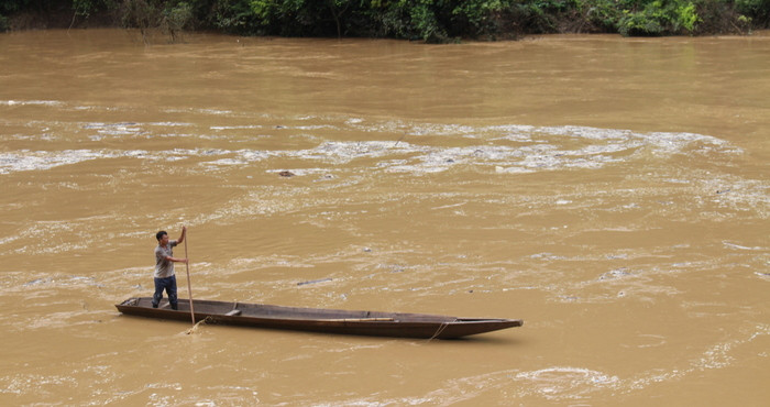 Người đàn ông này đang chèo thuyền ra sông chờ sẵn khi có củi, gỗ trôi đến sẽ vớt. Ảnh: Đình Tuân