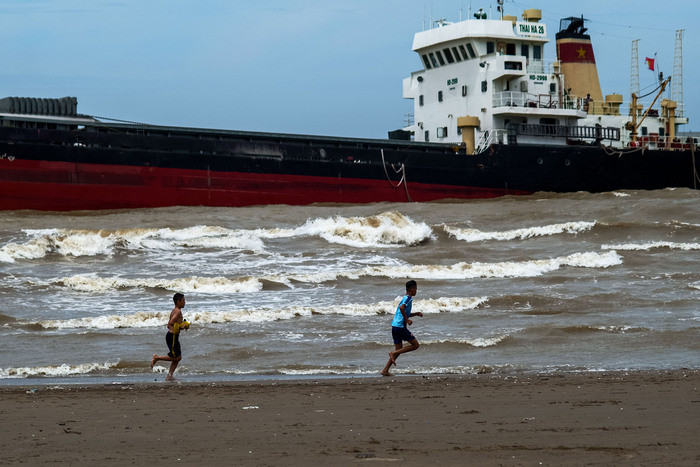 Hai người đàn ông chạy thể dục buổi sáng trên bãi cát, bên cạnh là con tàu hàng 