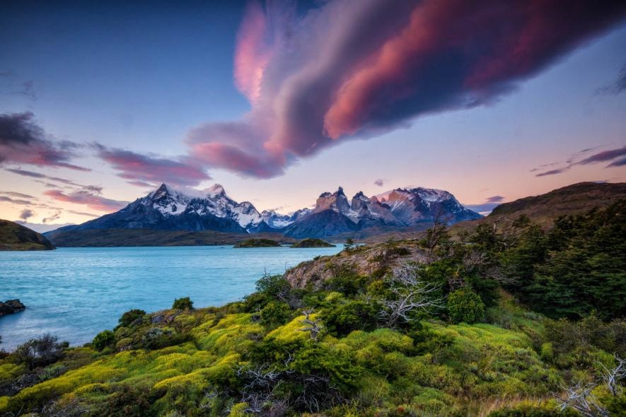 Dãy Andes nổi bật trên nền trời hồng và khung cảnh xanh tươi của công viên quốc gia Torres Del Paine, Chile.