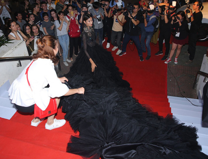 Hoàng Thùy diện bộ váy đen xếp nhiều tầng dài quét sàn. Cô có người trợ giúp khi di chuyển trên thảm đỏ.