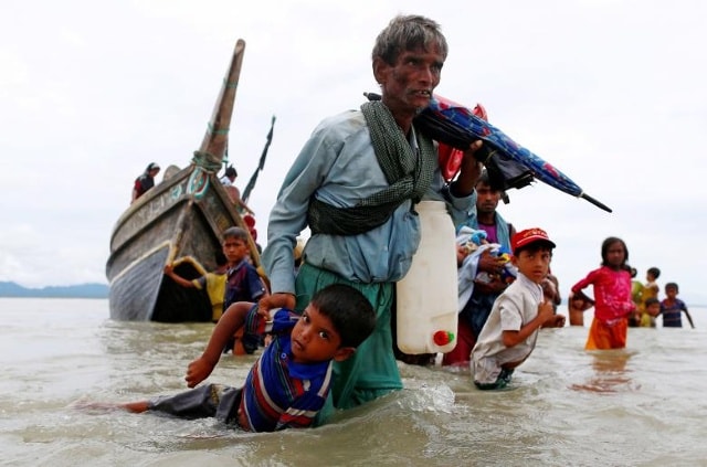 Một người đàn ông tị nạn Rohingya kéo một đứa trẻ khi họ đi bộ tới bờ sau khi băng qua biên giới Bangladesh-Myanmar bằng thuyền qua Vịnh Bengal ở Shah Porir Dwip, Bangladesh.