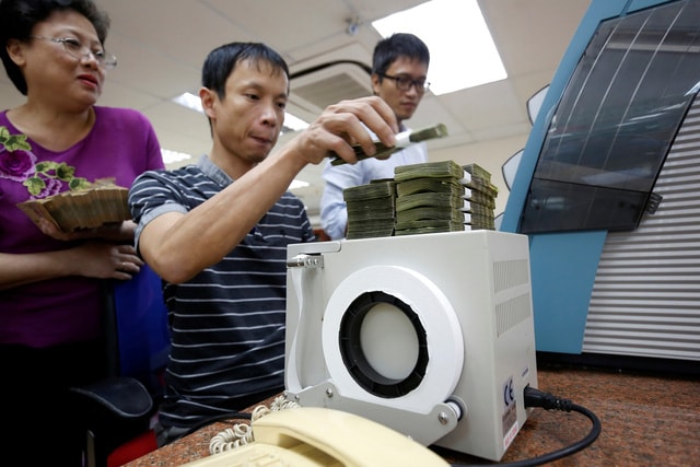 Người dân đếm tiền tại một chi nhánh ngân hàng ở Hà Nội - Ảnh: REUTERS