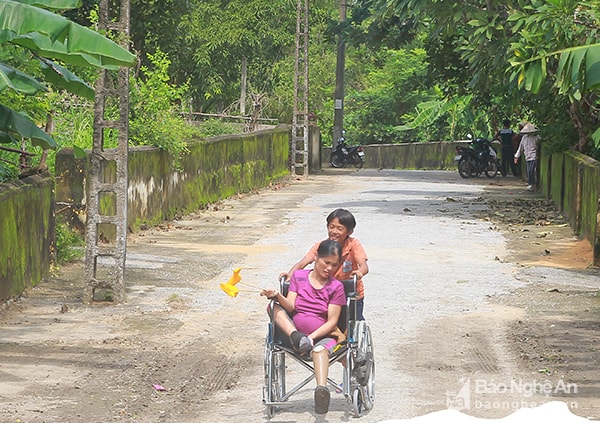 Ngồi trên chiếc xe lăn, chị Mai được con trai đẩy đến sân sinh hoạt chung của làng. Nếu không biết câu chuyện của chị, không ai ngờ đứa con trai tình cảm, quan tâm từng li từng tý đến mẹ lại không phải là con ruột của chị Mai. Bắt đầu phát bệnh từ lúc 14 tuổi, đến lúc bệnh nặng, phải cưa chân, chị mới biết mình mắc bệnh phong. Ảnh: Chu Thanh