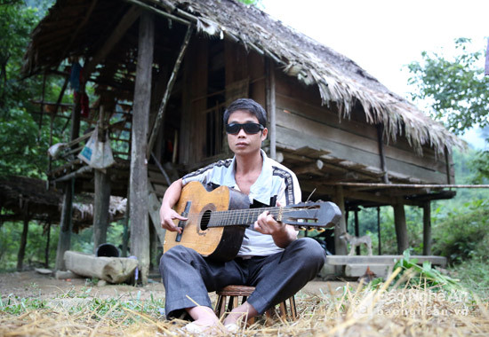 Anh La Văn Bồ đang ngồi đánh đàn bên căn chòi nhỏ của gia đình mình ở giữa rừng. Ảnh: Hồ Phương