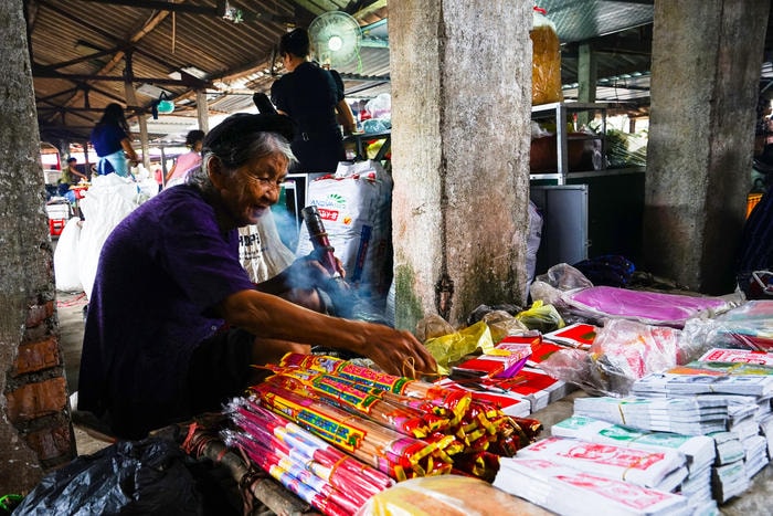 Một bà lão bán vàng mã ngồi thảnh thơi hút thuốc lào. Ảnh: Trung Hà