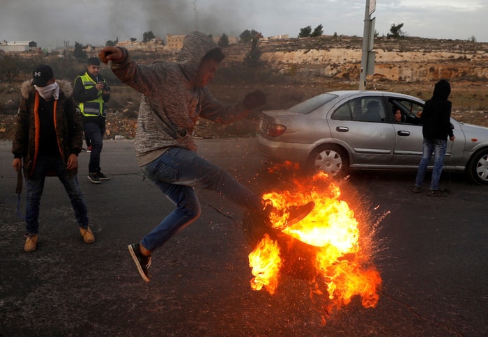 Người biểu tình Palestine đá một vỏ xe được châm lửa về phía binh sĩ Israel tại thành phố Ramallah, khu Bờ Tây ngày 10/12.  Ảnh: REUTERS