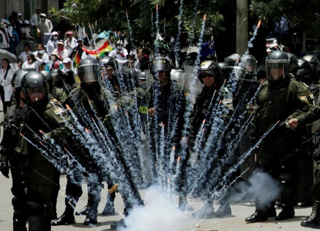 Pháo nổ phát nổ bên cạnh các nhân viên cảnh sát chống bạo động trong cuộc biểu tình phản đối chính sách chăm sóc sức khoẻ mới của chính phủ Bolivia ở La Paz, Bolivia vào ngày 27 tháng 12 năm 2017