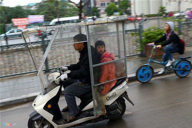 Một phụ huynh lắp thêm khung kính quây quanh xe máy che chắn gió đưa học sinh đến trường.