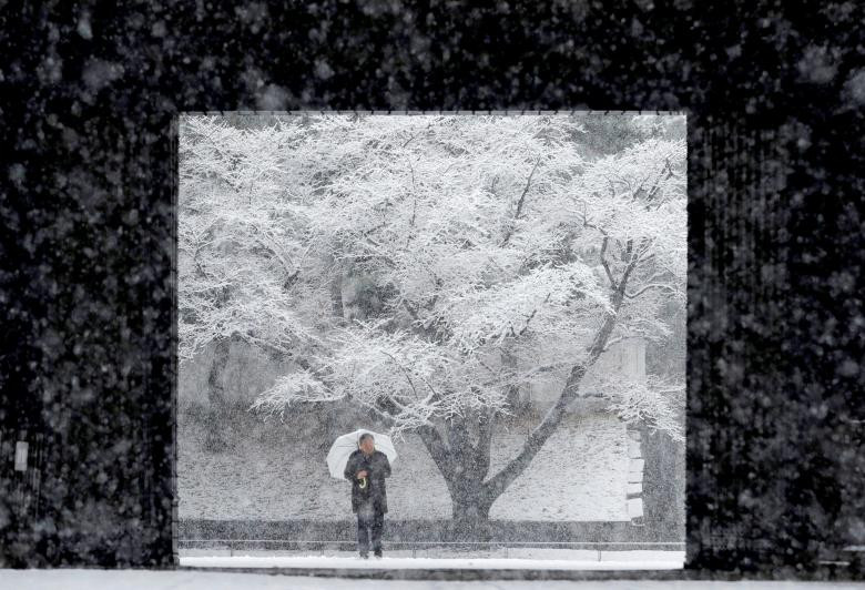 Một người đàn ông đang cầm một cây dù đang băng qua đường tuyết rơi tại Cung điện Hoàng gia ở Tokyo, ngày 22 tháng 1 năm 2018.