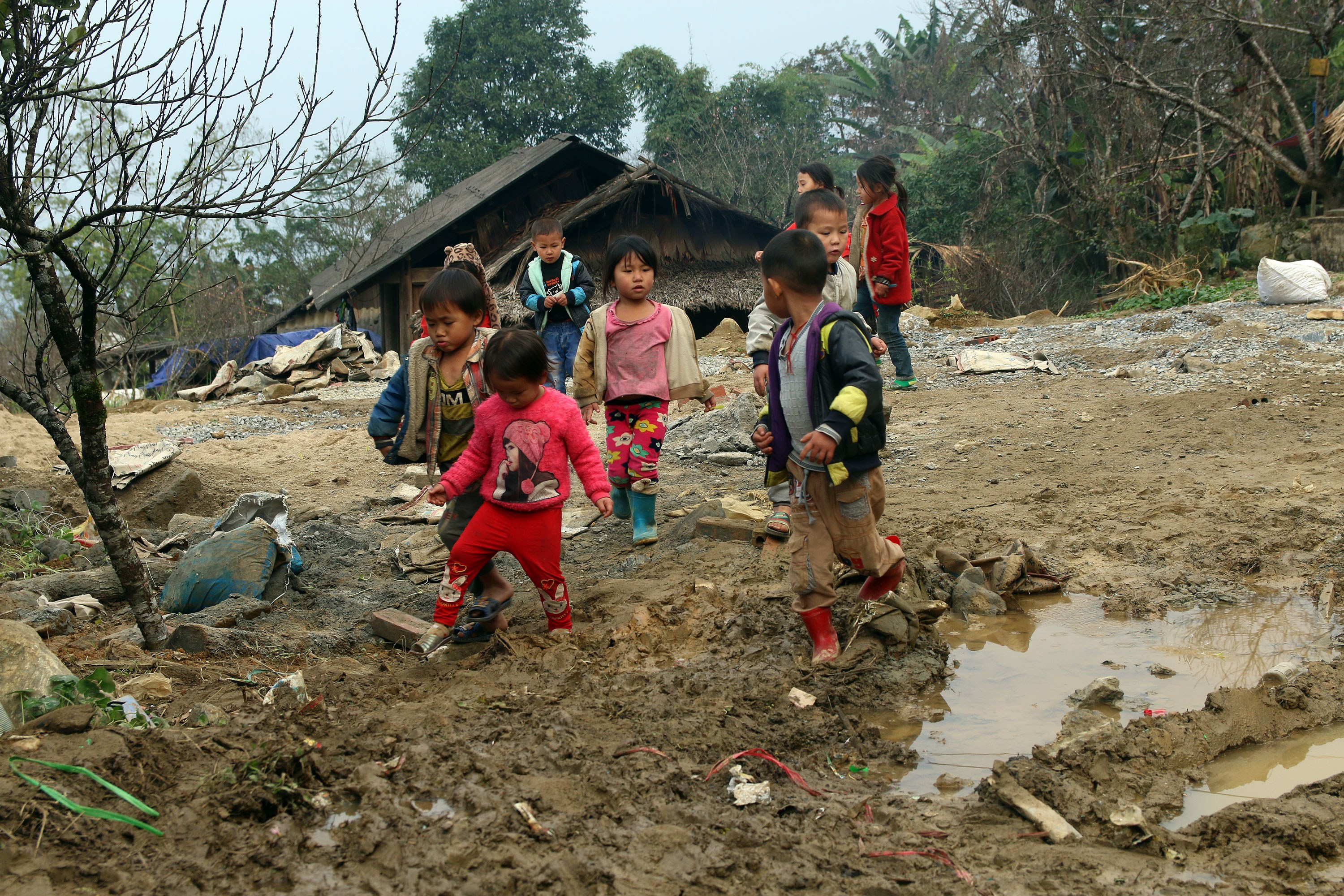 Những đứa trẻ người Mông quần áo mong manh chơi bên bãi đất trống bùn lầy ở bản. Ảnh: Đào Thọ