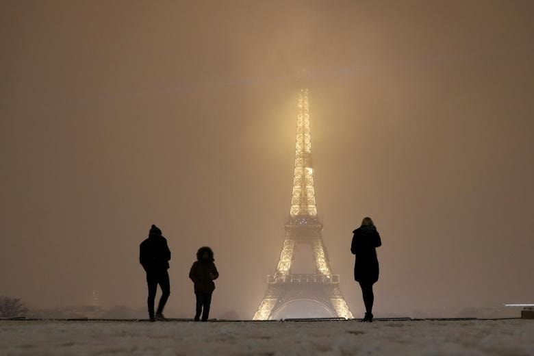 Khách du lịch chụp ảnh khi họ đi trên một con đường phủ tuyết gần tháp Eiffel ở Paris, khi thời tiết mùa đông đến tại Pháp