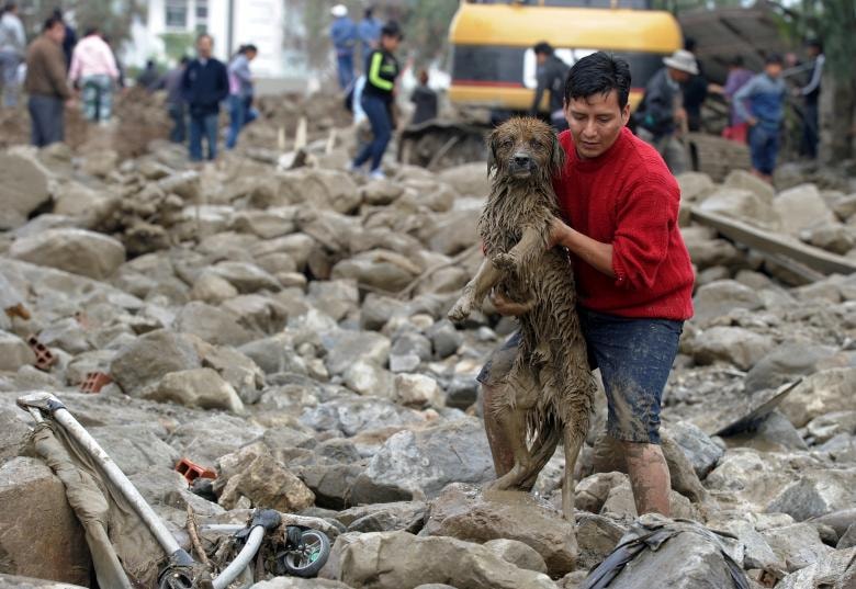 Một người đàn ông mang một con chó từ bùn và đá sau khi một con sông tràn ngập Tiquipaya do mưa lớn, ở Tiquipaya, Cochabamba, Bolivia.