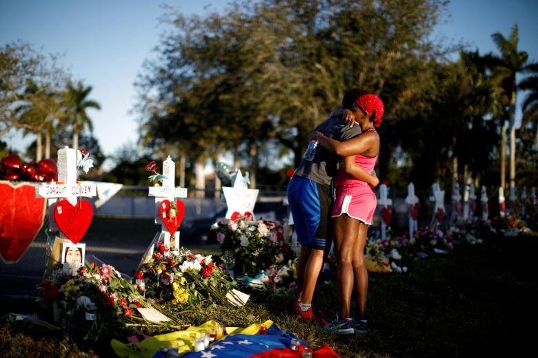 Adin Chistian (16 tuổi), học sinh của trường trung học Marjory Stoneman Douglas, bao bọc Denyse mẹ, bên cạnh cây thập tự và ngôi sao David đặt trước hàng rào của trường để kỷ niệm các nạn nhân của một vụ bắn súng tại Parkland, Florida.
