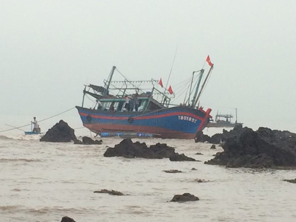 Chiếc tàu cá bị nạn nằm ngả nghiêng trên dãy đá sau thủy triều xuống.
