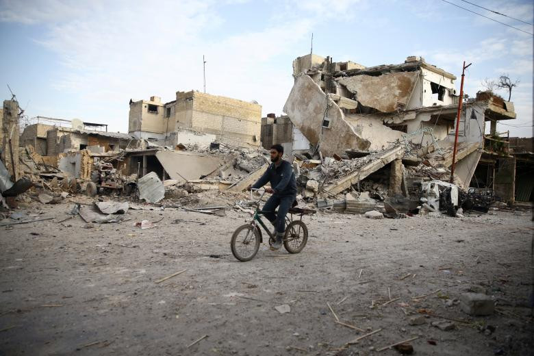 Một thanh niên lái xe đạp gần những ngôi nhà bị hư hỏng ở thị trấn Douma, Đông Ghouta, Damascus, ngày 20 tháng 2. 