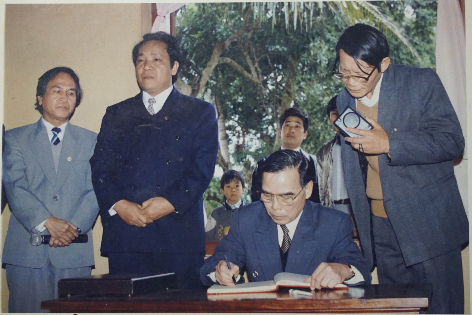 Thủ tướng Phan Văn Khải ghi sổ lưu niệm tại Khu di tích Kim Liên trong lần về thăm và làm việc tại Nghệ An năm 1998 (nhà báo Văn Hiền đứng ngoài cùng bên phải). Ảnh: Sỹ Minh