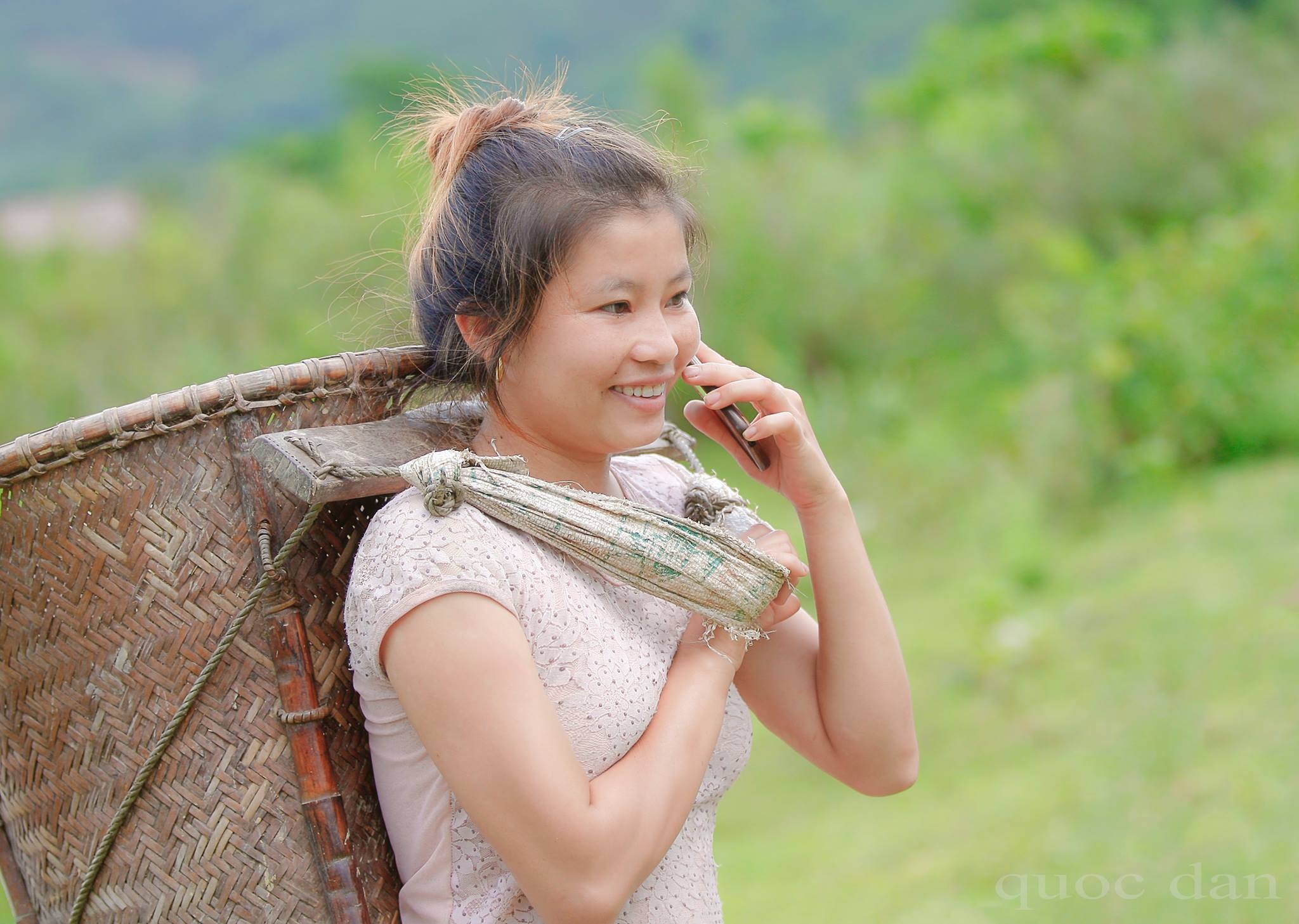 Một cô gái mang gùi vào rừng, trên tay đang cầm điện thoại di động để nói chuyện với bạn. Ảnh: Quôc Đàn