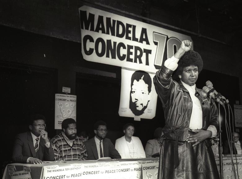 Winnie Mandela giơ tay lên trong màn chào hỏi của một người da đen sau khi thông báo rằng một buổi hòa nhạc pop lớn sẽ được tổ chức để đánh dấu ngày sinh nhật 70 của chồng Nelson Mandela, vào năm 1988