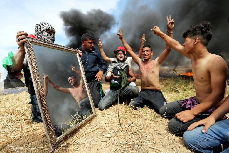 Các nhà hoạt động Palestine được nhìn thấy phản ánh trong gương khi họ tụ tập tại biên giới Israel-Gaza, ở dải Gaza phía Nam. 